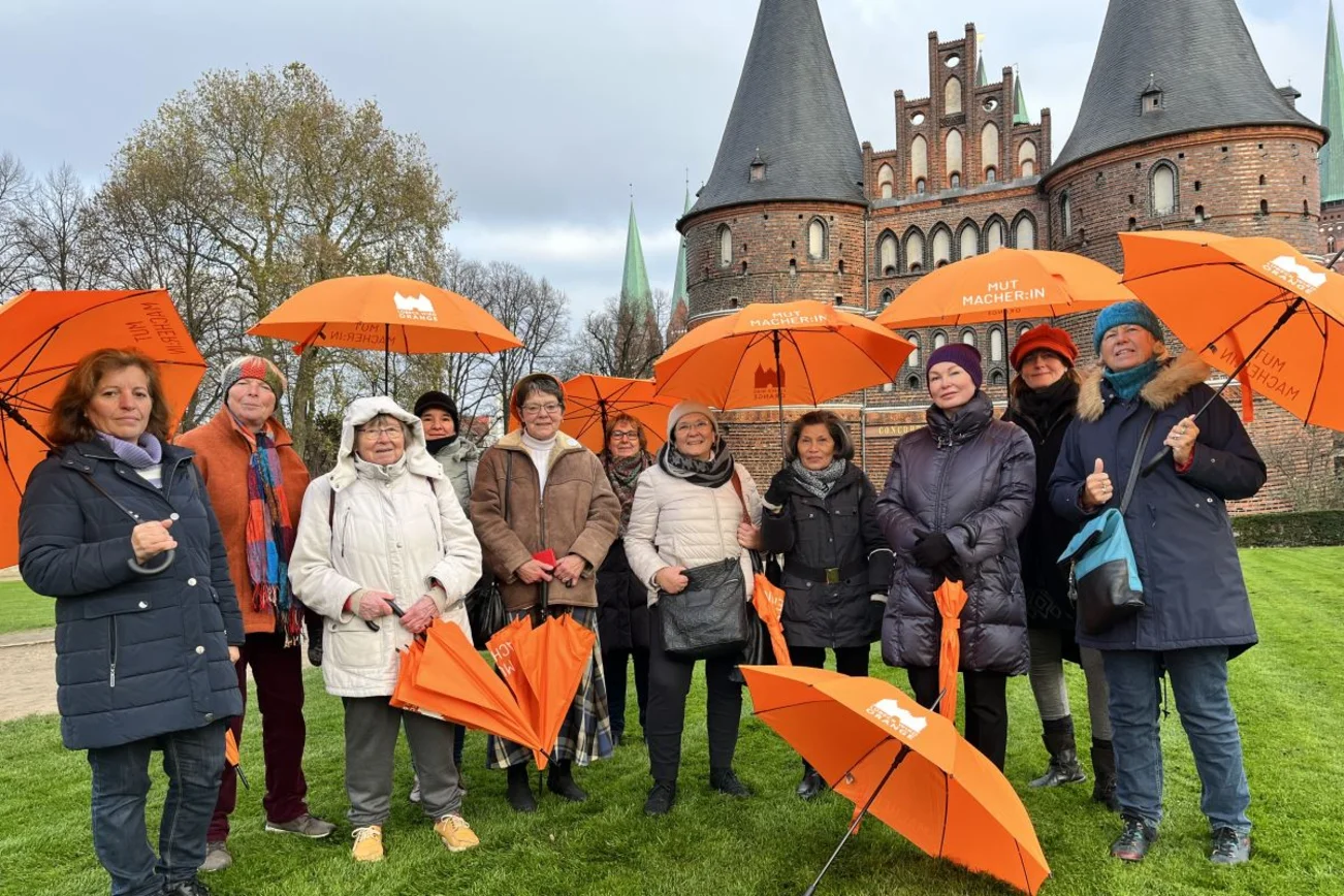 Frauen mit orangefarbenen Regenschirmen vor dem Holstentor in Lübeck
