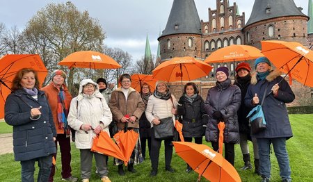 Frauen mit orangefarbenen Regenschirmen vor dem Holstentor in Lübeck