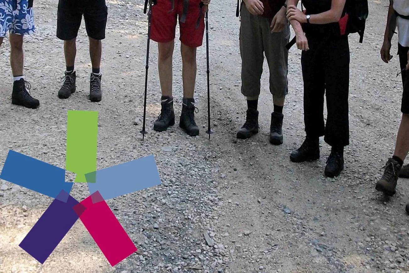 im Halbkreis stehende Leute mit Wanderstöcken, links unten das bunte Windrad