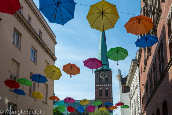 Aufgespannte Regenschirme in verschiedenen Farben, an mehreren Seilen aufgehängt - Im Hintergrund St. Jakobi Lübeck - Copyright: Monika Glende