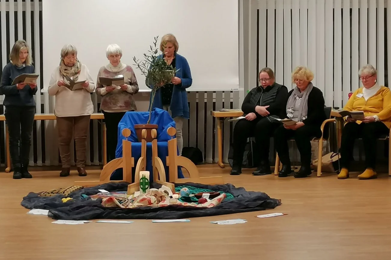 Frauen sitzen am Rand eines Raumes, in der Mitte liegt das WGT-Logo