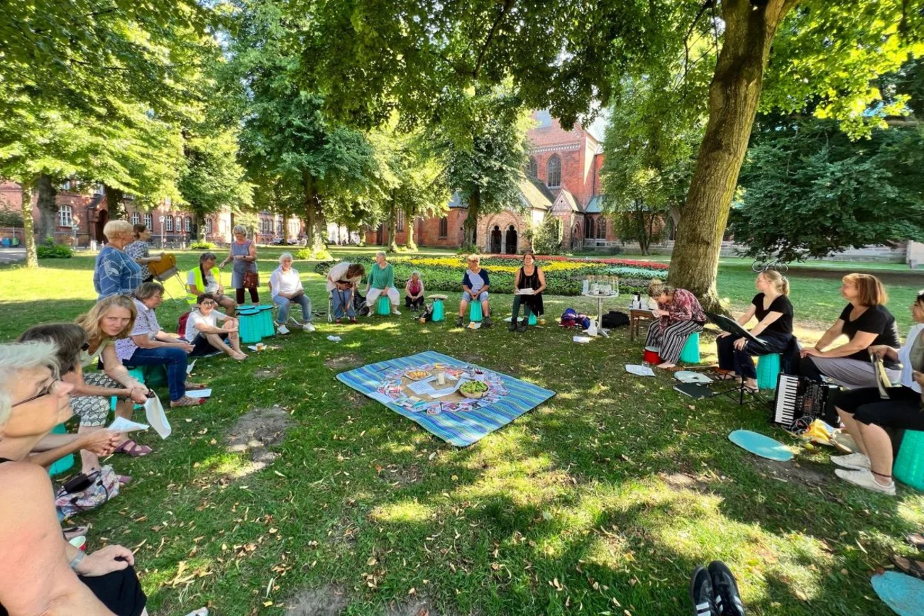 viele Personen sitzen im Kreis auf einer Wiese