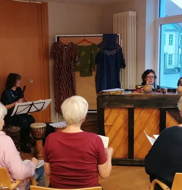 Frauen sitzen im Halbkreis um ein Klavier